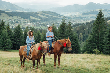 a couple horseback riding from overlooking wide open field and mountains