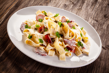 Pasta with cream sauce and sausages on wooden background