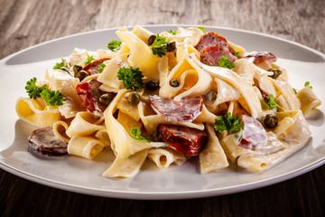 Pasta with cream sauce and sausages on wooden background