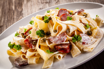 Pasta with cream sauce and sausages on wooden background