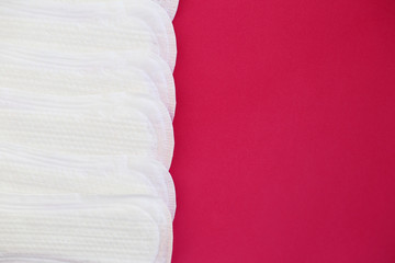 Protective white pads laid out in a row for woman hygiene and care on bright pink background for using in days of menstrual mothly cycle.