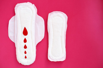 White woman cotton menstruation pads of different sizes with wings with red paper drops on pink background.