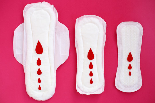 White woman cotton menstruation pads of different sizes with wings with red paper drops on pink background.
