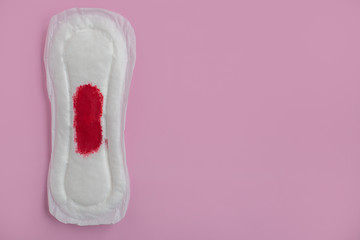 Slim cotton menstruation pad with red blood spot on pink background