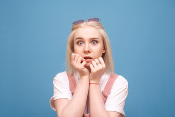 Close-up portrait of a blond girl with a shocking face looks at the camera on a blue background.Frightened lady is shocked looking at the camera, isolated on a blue background