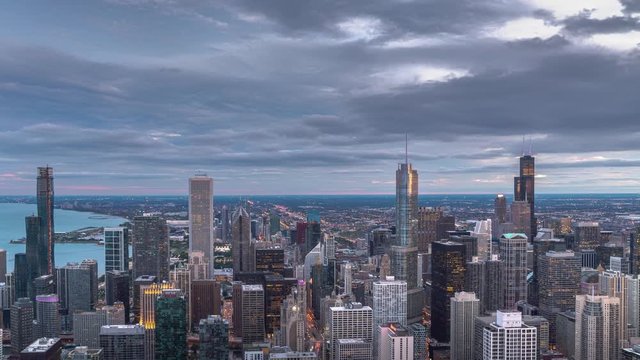 A beautiful aerial skyline panoramic sunset day to night zoom in time lapse of downtown Chicago with Lake Michigan and colorful pink and blue clouds as the sun sets and lights come on in the city.