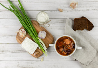 red borsch, a traditional national dish of Ukrainian cuisine. on the stock photo is served in a white plate with sour cream, green onions and garlic on a light wooden background using gray textile