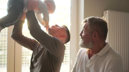 Grandfather with son and grandson smiling sitting on the couch. The adult son raises the grandson above the head. three generations of men of the same happy family. Father's Day, Indoor Portrait