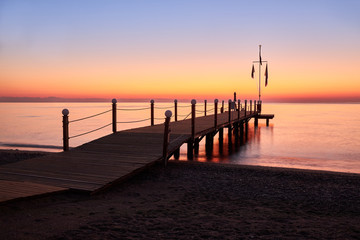 Calm warm sea and a large wooden pier with a swimming area at dawn