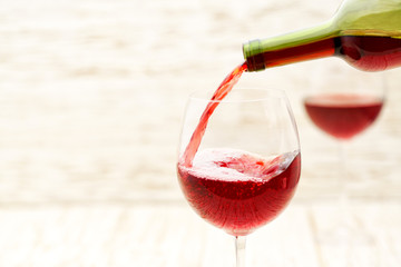 Pouring red wine into the glasses against  white wooden background