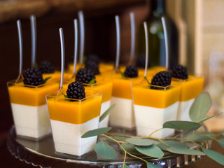 Yellow and white gel desserts with blackberries decorated with eucalyptus branches and with spoons in them