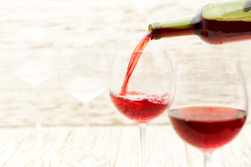 Pouring red wine into the glasses against  white wooden background