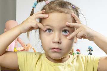 little girl holding hands on her head, she is in the room behind her toys