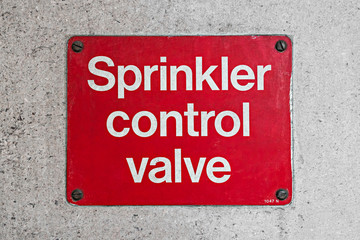 Simple bright red and white SPRINKLER CONTROL VALVE sign affixed to a wall.