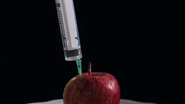 Syringe stuck in apple on plate isolated in black background