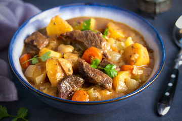 Beef meat stewed with potatoes, carrots and spices in bowl on dark gray background.  horizontal image