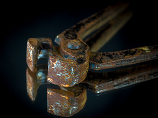 Old rusty iron pincer on a mirror with a black background