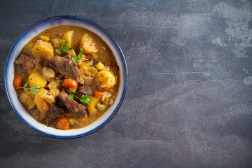 Beef meat stewed with potatoes, carrots and spices in bowl on dark gray background. Overhead...