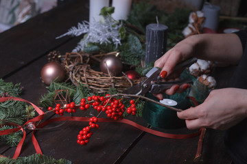 Close-up of a female florist making a Christmas wreath of fir branches, Christmas bubbles and natural decor, selective focus