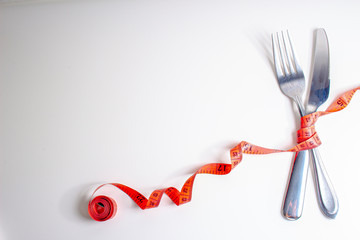 Lose weight. A fork and knife are wrapped in a red measuring tape on white background on the right