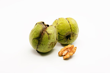 Close up shot of two raw wallnuts with green shell and one piece of walnut near to them.