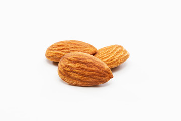 Close up shot of three roasted almonds on a white background.