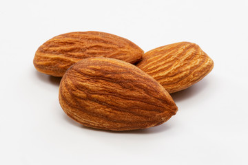 Close up shot of three roasted almonds on a white background.
