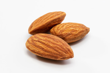 Close up shot of three roasted almonds on a white background.