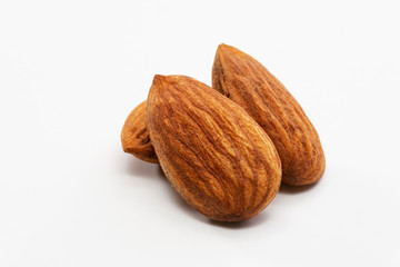 Close up shot of three roasted almonds on a white background.