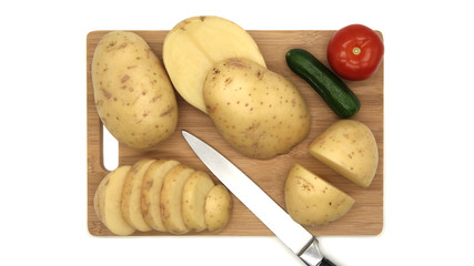 Board with fresh, raw vegetables, top view. Knife, board, tomato, cucumber.        Isolated objects on a white background. Young white potato.   Fresh food for vegetarians. Raw vegetable, root vegetab