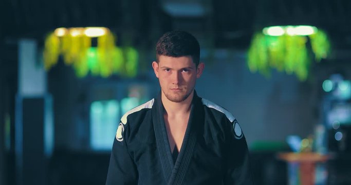 Male athlete in a black kimono looks at the opponent, a serious look. Young male judoka is attuned to battle. Portrait view.