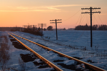 Railway Tracks and Telegraph Poles with Snow under Orange Sunset Sky