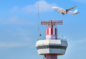 Radar  air traffic control tower in international airport while airplane taking off under blue sky.                 