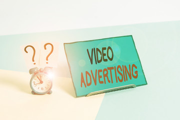 Writing note showing Video Advertising. Business concept for encompasses online display advertisements that have video Alarm clock beside a Paper sheet placed on pastel backdrop
