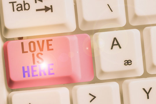 Handwriting text Love Is Here. Conceptual photo Roanalysistic feeling Lovely emotion Positive Expression Care Joy White pc keyboard with empty note paper above white background key copy space