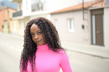 Portrait of an afro-style black girl with long black curly hair standing on the street, looking at the camera