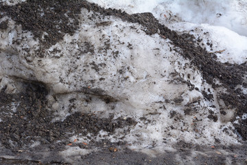 Close up of dirty snow pile covered in soil from repeated plowing during and after snow storm