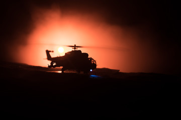 Fototapeta premium Silhouette of military helicopter ready to fly from conflict zone. Decorated night footage with helicopter starting in desert with foggy toned backlit. Selective focus.