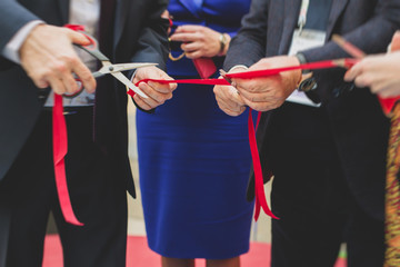 Process of cutting the red ribbon during the grand opening of the new shopping center mall building, opening of exhibition, close up view of red ribbon with people around