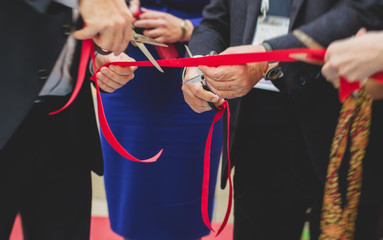 Process of cutting the red ribbon during the grand opening of the new shopping center mall building, opening of exhibition, close up view of red ribbon with people around