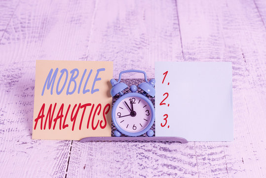 Conceptual hand writing showing Mobile Analytics. Concept meaning studies the behavior of mobile website visitors and users Mini blue clock standing above buffer wire between two paper