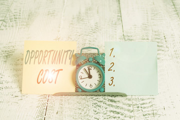 Conceptual hand writing showing Opportunity Cost. Concept meaning the price of the next best thing you could have done Mini blue clock standing above buffer wire between two paper