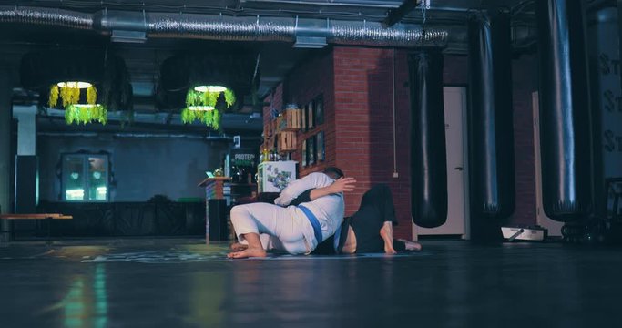 Fighters are fighting in the gym, painful technique. Men judokas practice tricks in training. Side span of the camera.