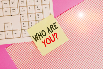 Text sign showing Who Are You question. Business photo text asking about demonstrating identity or information Note paper stick to computer keyboard near colored gift wrap sheet on table