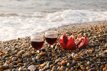 Ripe pomegranate fruit with a glass of wine on the beach. The concept of the wedding or the celebration of Valentine day.