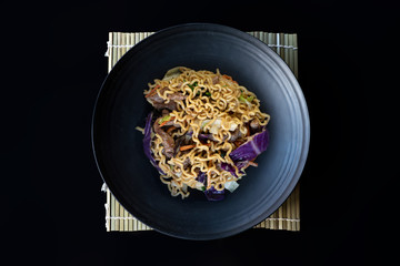 Stir fry noodles with vegetables and beef in black bowl.