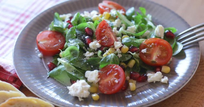 Fresh made arugula salad with cherry tomatoes, soft cheese, sweetcorn kernel and pomegranate seed on plate on rotating stand, close up