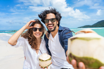 Beautiful young couple joyfully on a tropical beach with coconuts in their hands on the seashore....