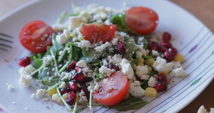 Fresh made arugula salad with cherry tomatoes, soft cheese, sweetcorn kernel and pomegranate seed on plate on rotating stand, close up