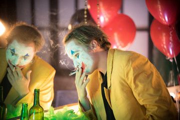 Clown concept - a tired sad man clown in yellow jacket smoking in the dressing room